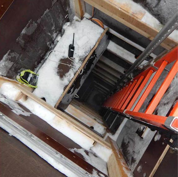 On a construction site, you look down into a deep shaft made of wood. A red ladder leads down the shaft. There is ice and snow at the top of the shaft; a radio is located at the entrance to the shaft.