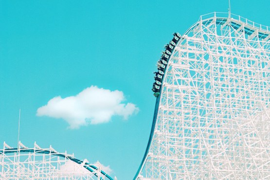 Against the background of the blue sky you can see the white structure of a roller coaster, which in this section drops steeply from top right to bottom left and is being ridden by an almost full car.