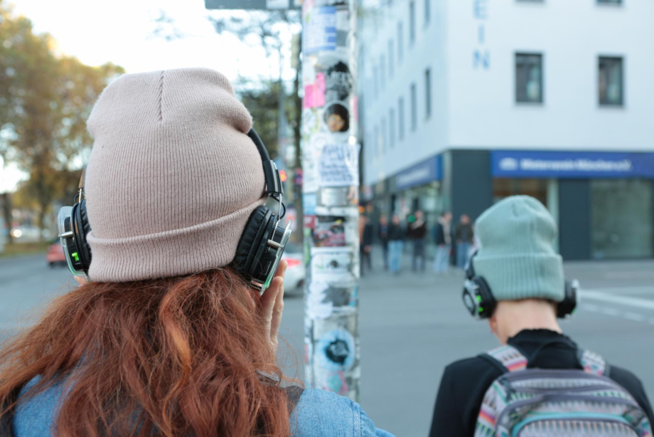 Two teenagers with hats and headphones are standing on a large street