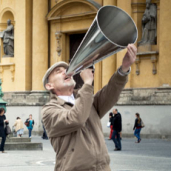 Ein älterer Mann mit großer Flüstertüte vor den Mund auf dem Odeonsplatz