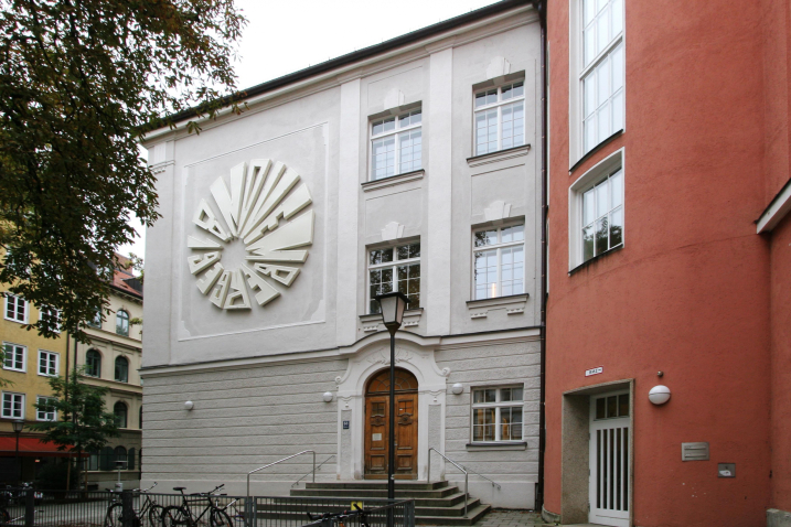 A large circular installation made of neon tubes is attached to a white house wall facade on the first floor, which gives the date "November 8, 1939".