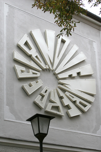 A large circular installation made of neon tubes is attached to a white house wall facade on the first floor, which gives the date "November 8, 1939".