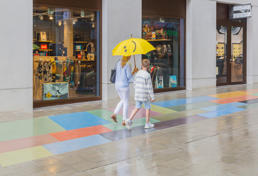 A young woman and a boy of about twelve walk along the ground monument. The woman holds a large yellow umbrella open in her right hand as it is raining lightly.
