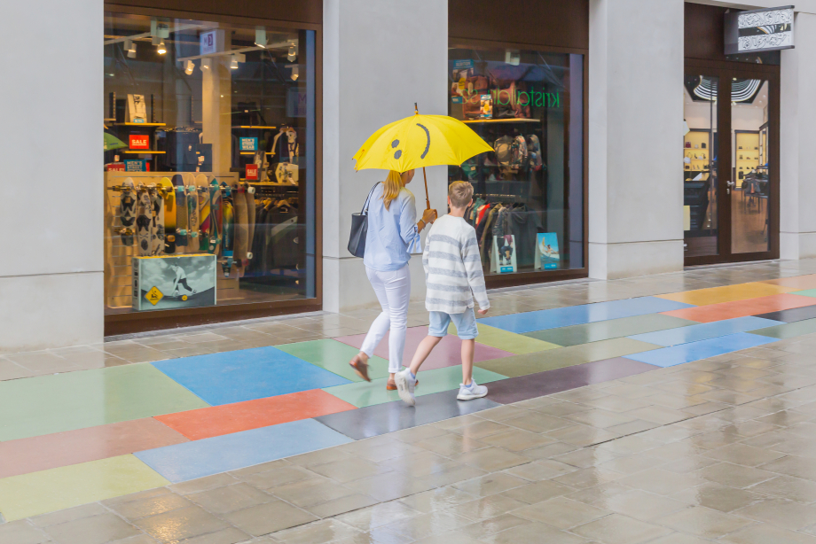 Eine junge Frau und ein etwa zwölfjähriger Junge gehen auf dem Bodendenkmal entlang. Die Frau hält einen großen gelben Regenschirm aufgespannt in ihrer rechten Hand, da es leicht regnet.