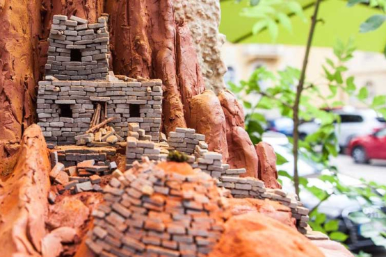 A small-format work of art can be seen on a ledge of a house. It shows tiny dwellings, in the Pueblo style, built of red clay and tiny bricks.