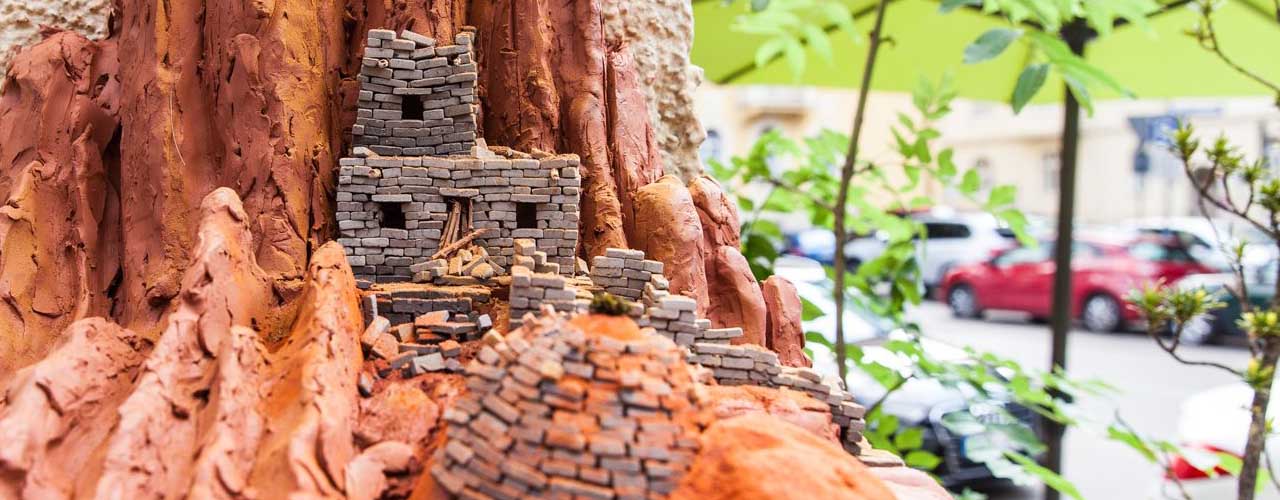 A small-format work of art can be seen on a ledge of a house. It shows tiny dwellings, in the Pueblo style, built of red clay and tiny bricks.