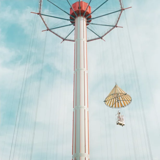 Vor dem Hintergrund des leicht bewölkten Himmels führt der Blick entlang einer riesigen Säule von unten nach oben. An einer kreisrunden Konstruktion am oberen Ende der Säule ist eine Art Gondel befestigt, die rechts in der unteren Hälfte des Bildes schwebt. Eine Person winkt von dort herab.