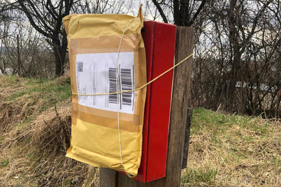 An old-looking mailbox in front of a meadow, to which a parcel is tied.