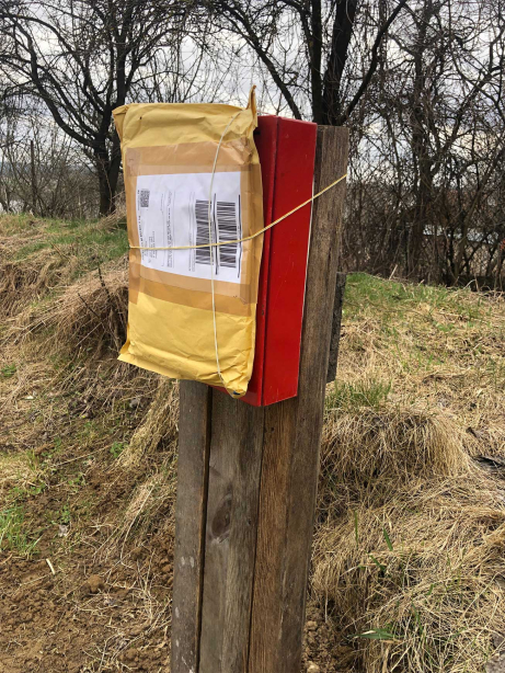 An old-looking mailbox in front of a meadow, to which a parcel is tied.