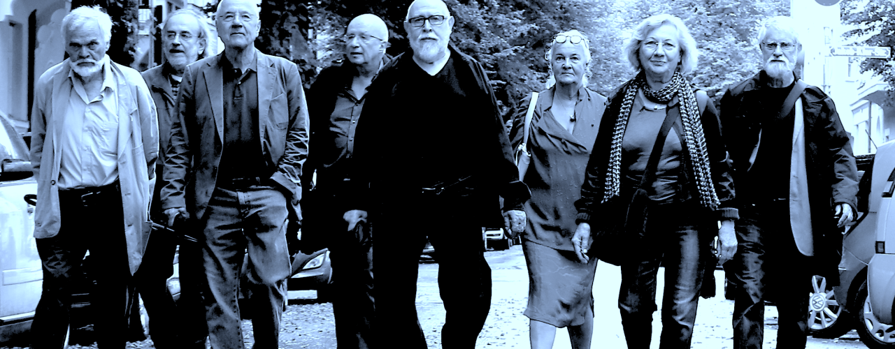 The black-and-white photo shows several elderly people walking towards the viewer on a rain-soaked street