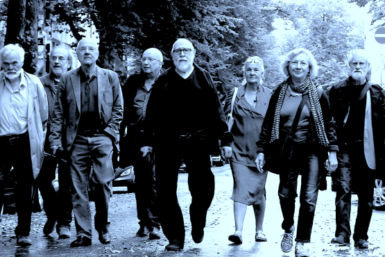 The black-and-white photo shows several elderly people walking towards the viewer on a rain-soaked street