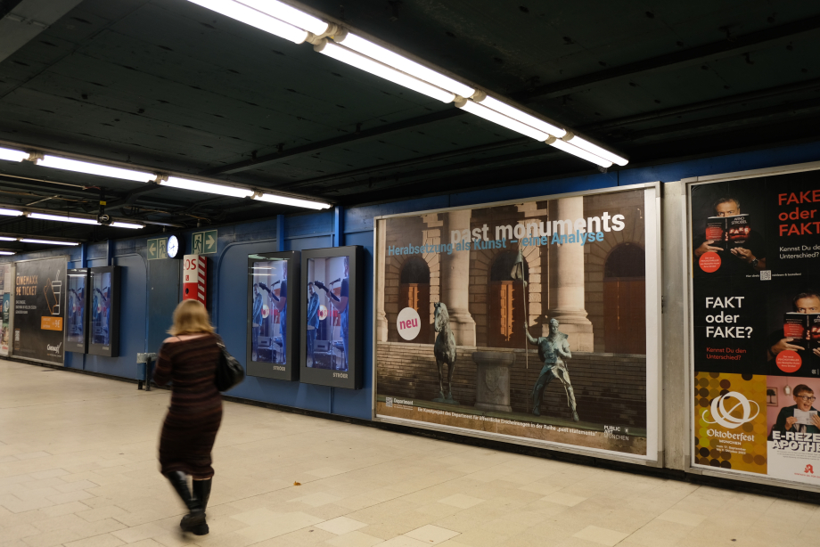 An underpass, on the walls various posters, the poster in the middle shows an equestrian statue, but horse and rider are to the left and right of the pedestal