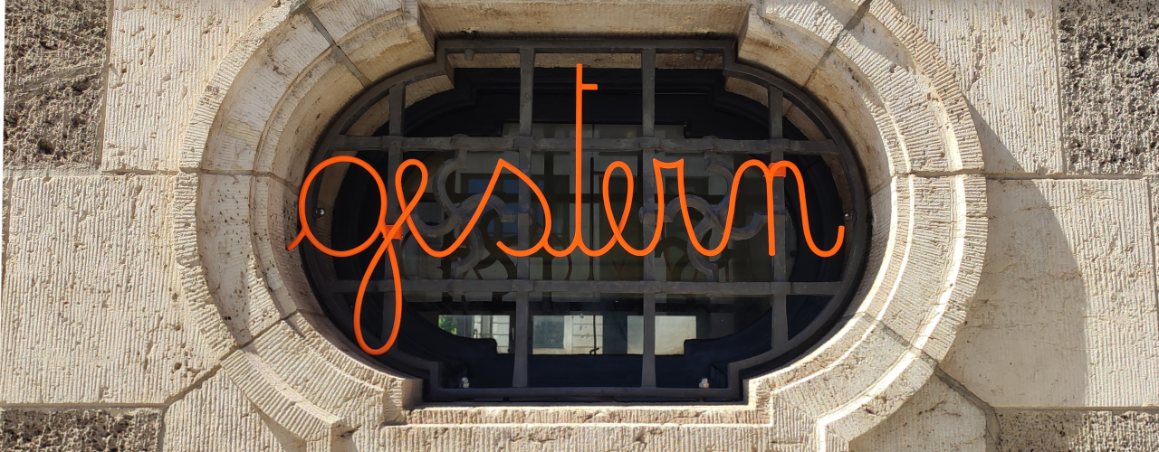 Orangefarbener Schriftzug "gestern" vor einem Fenster, auf dem sich das Fresko eines Hakenkreuzes befindet.