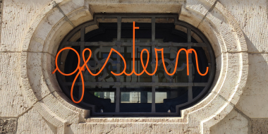 Orangefarbener Schriftzug "gestern" vor einem Fenster, auf dem sich das Fresko eines Hakenkreuzes befindet.