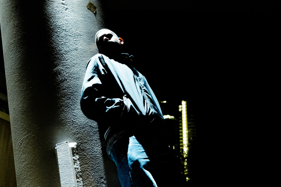 Nocturnal photo of a youth leaning against a wall, the face partly in the light, partly illuminated, is not recognisable