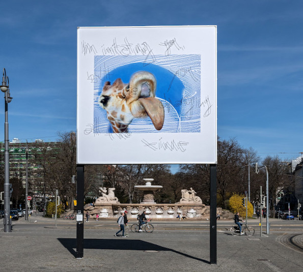 Frontal view of the billboard against blue sky. The motif shows a giraffe that seems to lick a glass window with its tongue. Above the image appears the text "I'm imitating you, but you are changing all the time".