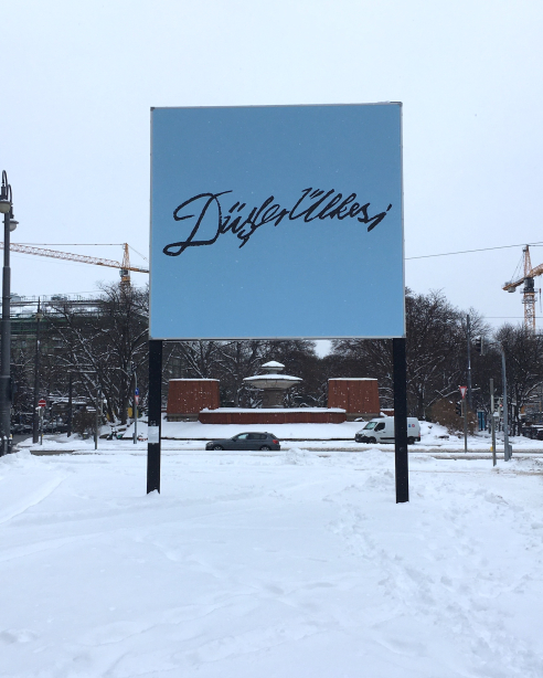 Frontale Ansicht des Billboards im Schnee. Das Motiv zeigt in schwarzer Schrift auf blauem Grund die Worte "Düşler Ülkesi", welche sich aus dem Türkischen wörtlich mit "Land der Träume" übersetzen lassen.