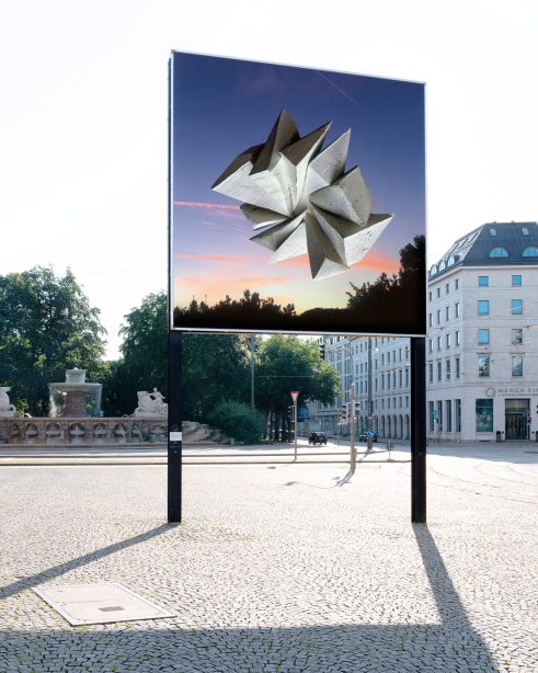 Diagonal view of the billboard side facing towards the city center. The motif shows an abstract stone formation floating above trees in front of a sunrise.