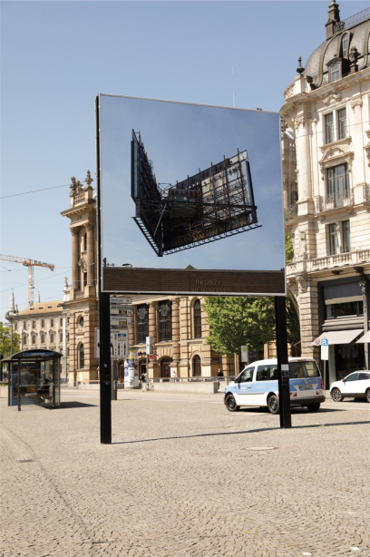 Slightly diagonal view of the billboard at Lenbachplatz. The motif shows the metal structures of the back of an advertising billboard. The billboard appears to float freely above a building below without any supporting structures.