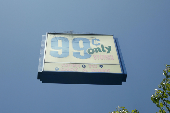 Das Motiv zeigt ein Werbebillboard mit der Aufschrift "99 Cents only stores" vor blauem Himmel, das ohne Stützstrukturen frei über der Erde zu schweben scheint.