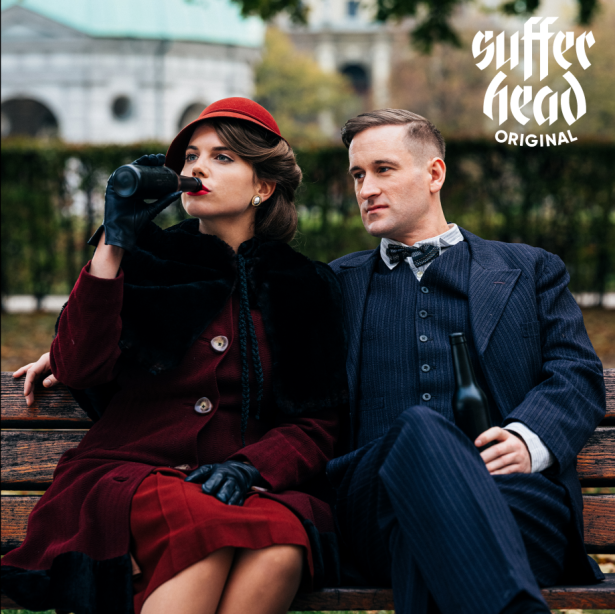 The billboard motif shows a woman and a man sitting on a park bench, both holding a beer bottle in their hands, the woman has brought hers to her lips to drink. On the left hand appears the lettering "Sufferhead Original".