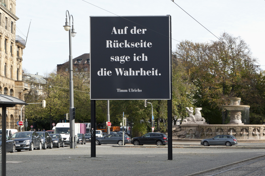Frontal view of the billboard. To be read in large white letters on a black background: "Auf der Rückseite sage ich die Wahrheit. Timm Ulrichs" ("I tell the truth on the reverse. Timm Ulrichs").