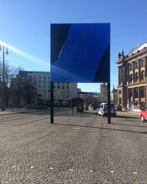 Frontal view of the billboard at Lenbachplatz. The motif shows a photograph of a plasterboard painted in black and royal blue. In some places, the brown backing material from inside the board is revealed.