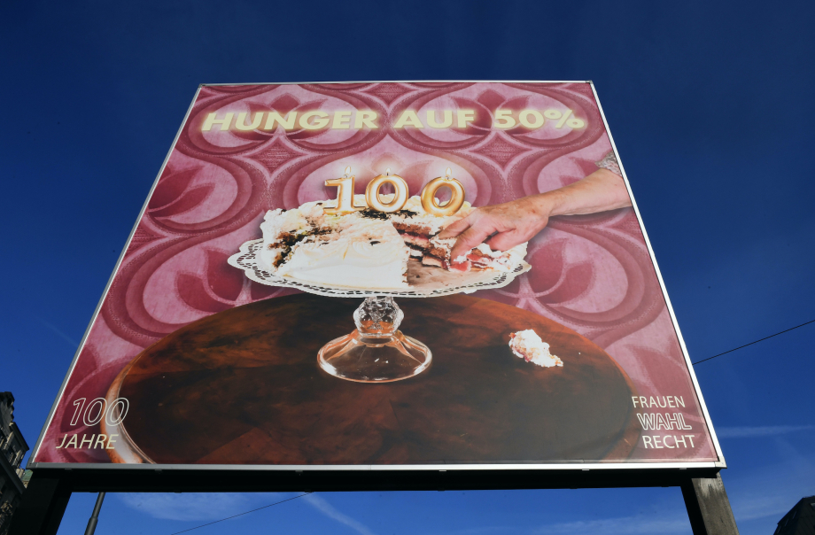 The motif shows a cream cake in the centre on a cake plate with burning birthday candles in the shape of a "100". A piece of the cake has been cut out, a hand is reaching for it. The text "Hunger auf 50%" ("Hungry for 50%") appears above it.