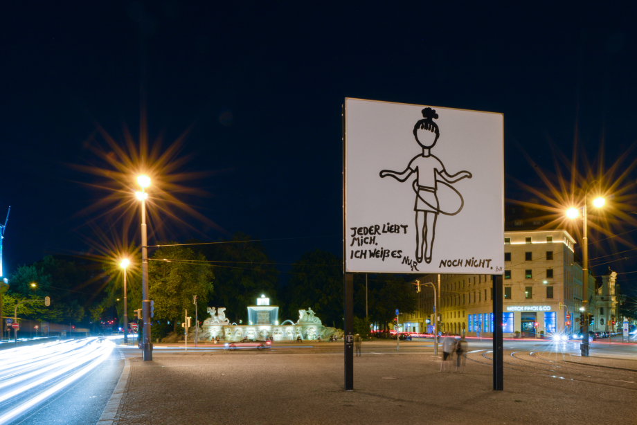 Side view of the billboard at Lenbachplatz in the evening hours. The motif shows a linear hand drawing of a girl swinging a hula hoop on a white background. The girl is depicted without a face. At the bottom of the image appears the writing: "Jeder liebt mich, ich weiß es nur noch nicht." ("Everyone loves me, I just don't know it yet.")