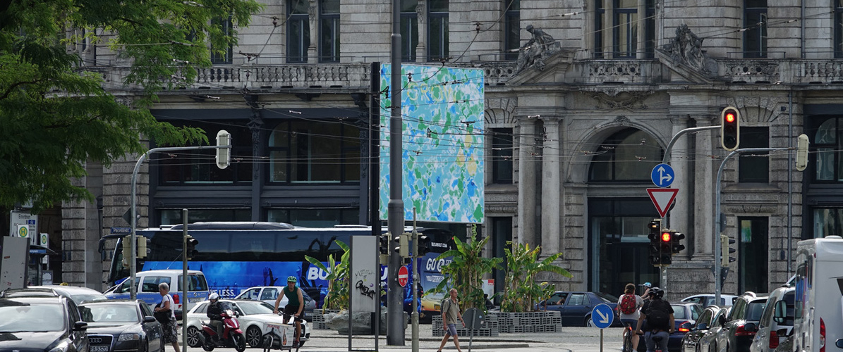 Side view of the billboard at Lenbachplatz from a distance during rush hour. The image shows an abstract blue-green sea. The word "GROW" appears in capital letters at the top of the image.