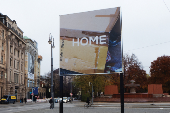 Diagonal view of the billboard. The motif shows cardboard boxes glued together to form a temporary canopy for housing.