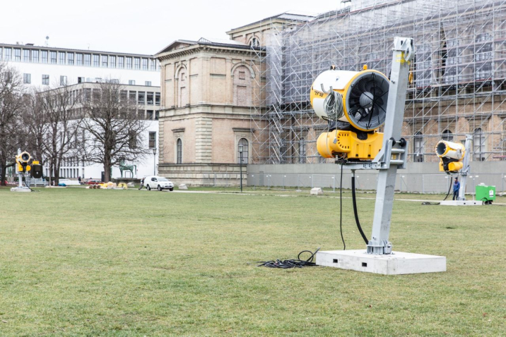 Three snow cannons arranged in a triangle stand on the green lawn in front of the Alte Pinakothek, which can be seen in the background.