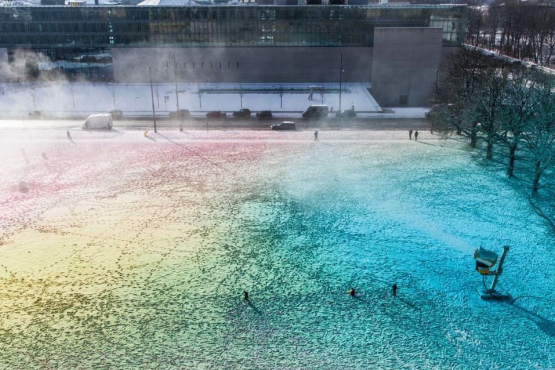 Blick von oben auf eine surreale bunte Schneefläche mit einer laufenden Schneekanone. Im Hintergrund zu sehen ist die Hochschule für Film und Fernsehen.