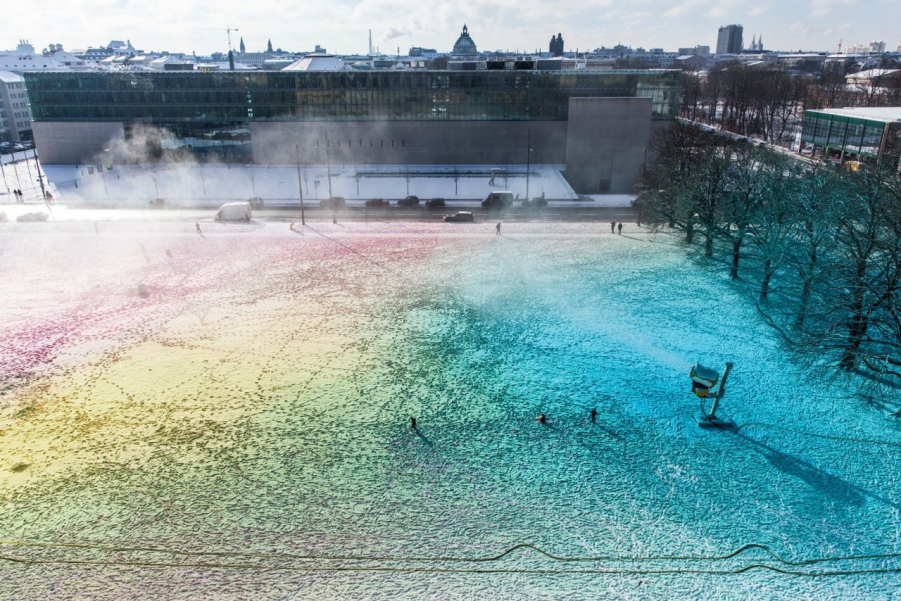 View from above onto a surreal coloured snowscape with a snow cannon in operation. In the background is the University of Film and Television (HFF).