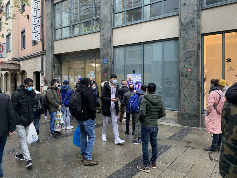 Street scene with passers-by grouped around a shop window.