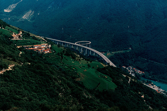 Fotocollage einer bewaldeten Landschaft mit einer Hochautobahnbrücke, die eine Schleife beschreibt.