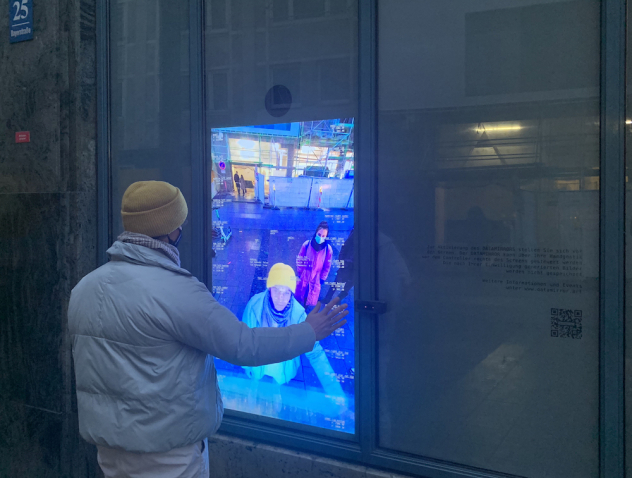 Back view of a man in a winter jacket and yellow cap. His face is reflected in a shop window, on which different coordinates also appear.