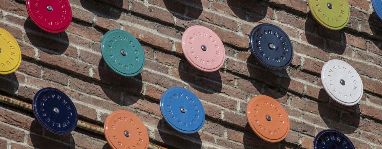 Nahaufnahme mehrerer verschiedenfarbig glasierter Keramikscheiben, die auf einer Backsteinwand angebracht sind.
