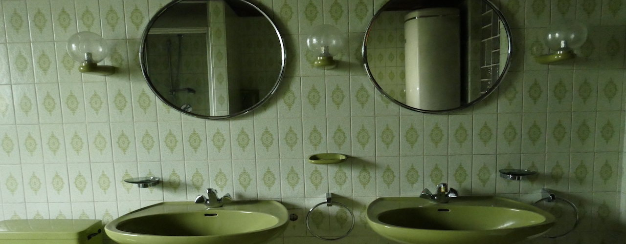 View of a green-tiled bathroom with two green washbasins in the centre and two round mirrors hanging above.