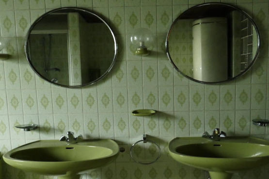 Blick in ein grüngefliestes Badezimmer, in der Mitte zwei grüne Waschbecken sowie zwei darüber hängende runde Spiegel.