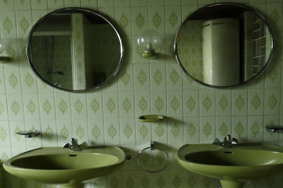 View of a green-tiled bathroom with two green washbasins in the centre and two round mirrors hanging above.