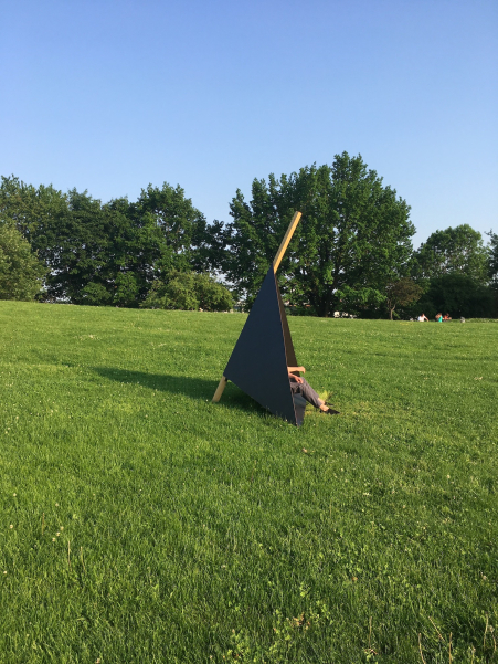 A man sits in a black triangular wooden construction as a seat on the meadow at Olympiaberg.