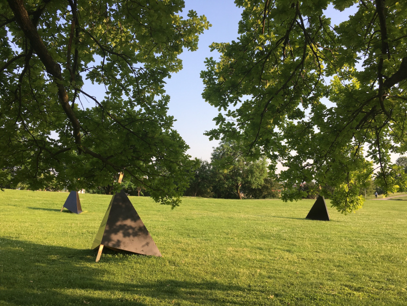 Three black triangular wooden structures can be seen as seating on the meadow on the Olympiaberg.