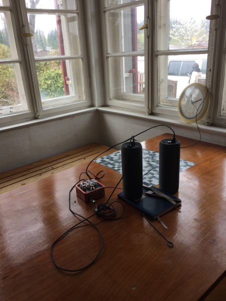 View into a kitchen room with a wooden table. On the table is a sound system with amplifiers and speakers connected to a clock.