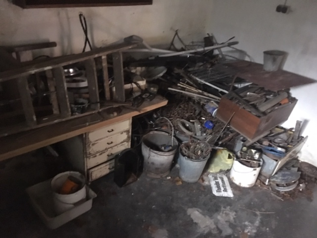 A view of a basement room full of junk, such as scrap iron in buckets, cables and old furniture.