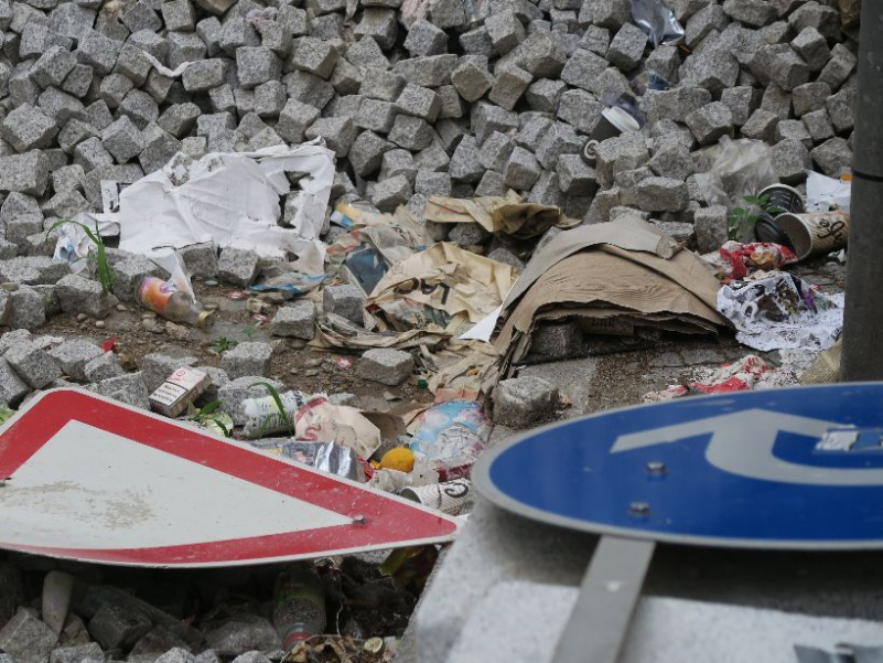 Zwei verbeulte Verkehrsschilder die im Unrat vor einem Haufen Pflastersteinen am Boden liegen.