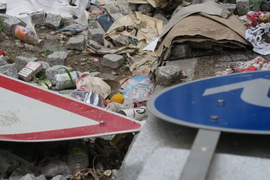 Two dented road signs lying in the garbage on the ground in front of a pile of cobblestones.