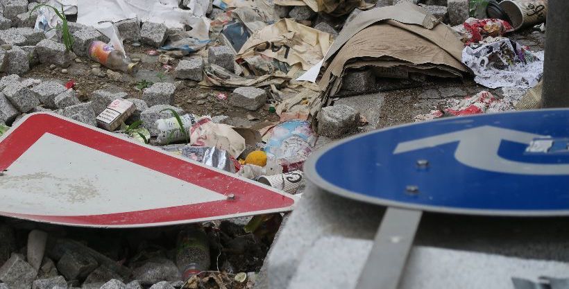 Zwei verbeulte Verkehrsschilder die im Unrat vor einem Haufen Pflastersteinen am Boden liegen.