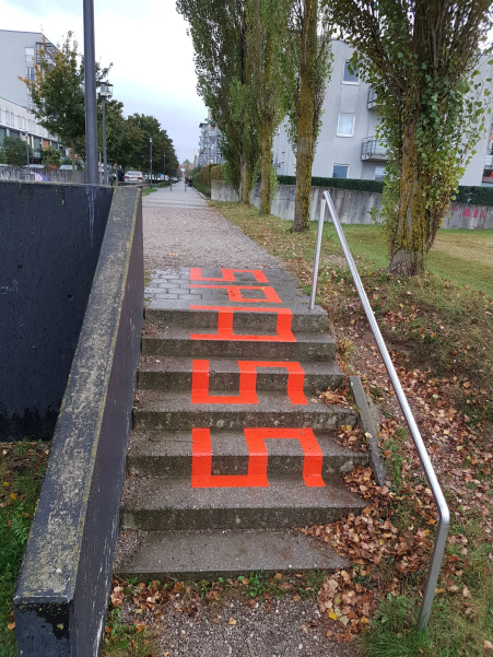 Zu einer mit Häusern gesäumten Straße führende Treppe mit zwei Handläufen. Auf die Treppe ist in roten Großbuchstaben das Wort "Spass" geklebt.