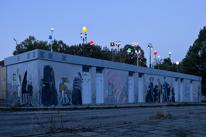 Verschiedene bunte Leuchten, montiert auf das Trambahn-Wartehäuschen am Ratzingerplatz in München in der Abenddämmerung.